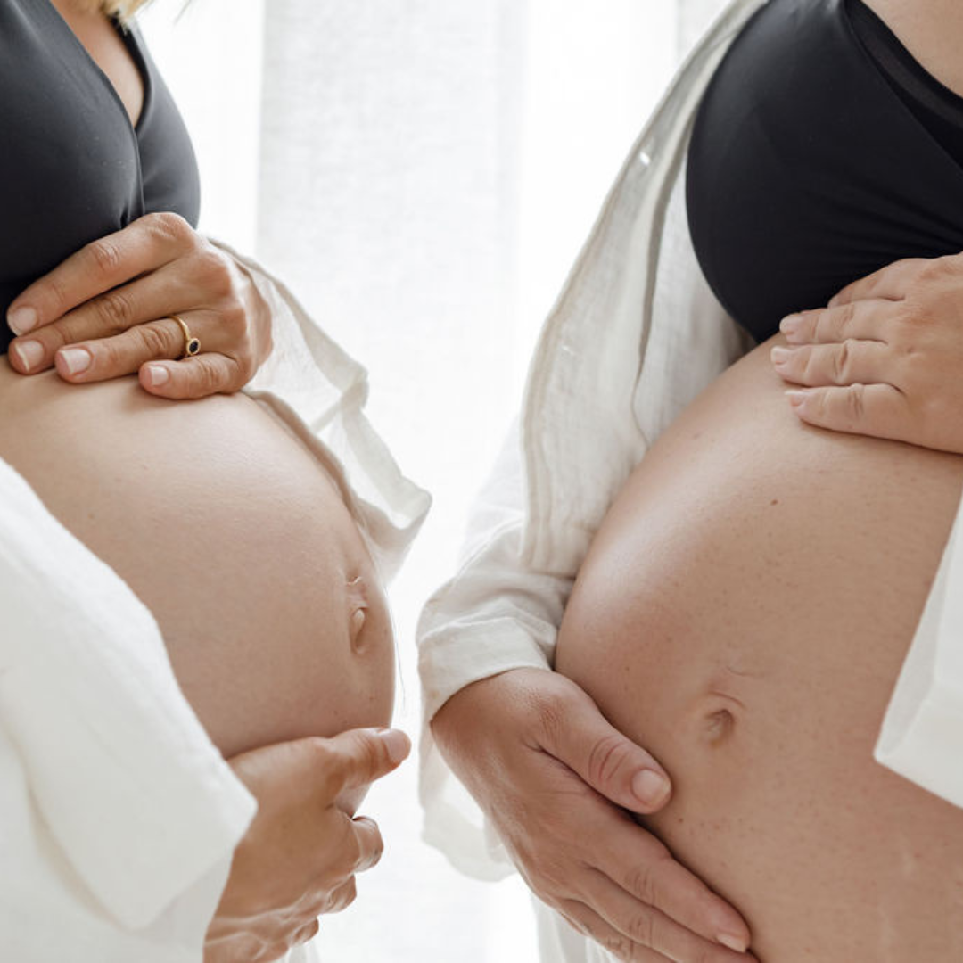 Two pregnant women in their third trimester put their bellies close to one another. They are large pregnant bellies getting ready for birth. 