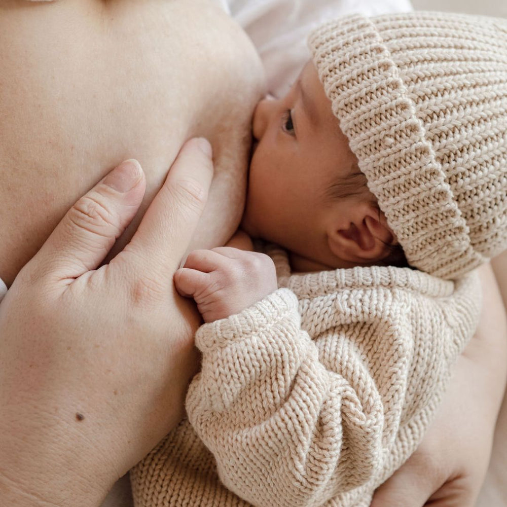 A close up image of a newborn baby breastfeeding. The mum is helping the baby latch to establish a strong breastfeeding connection. 