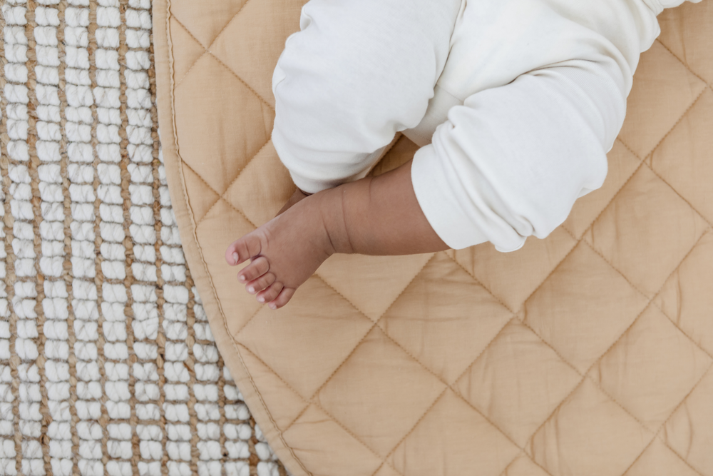 A baby's feet on a tan quilted mat.