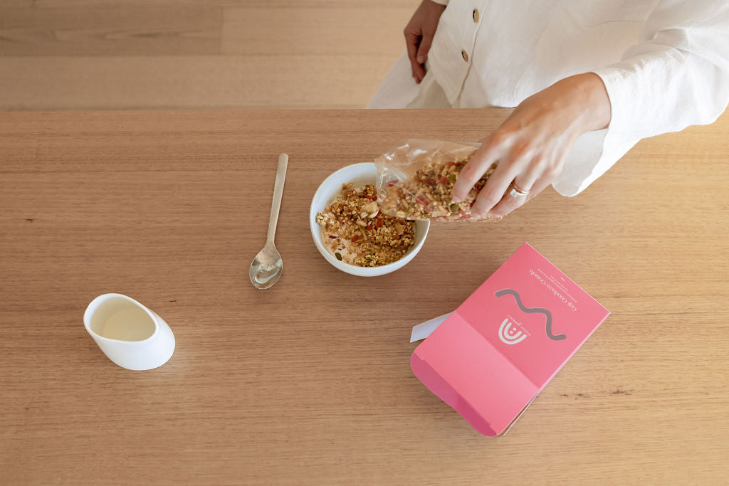 A woman pouring granola into a bowl on a table.