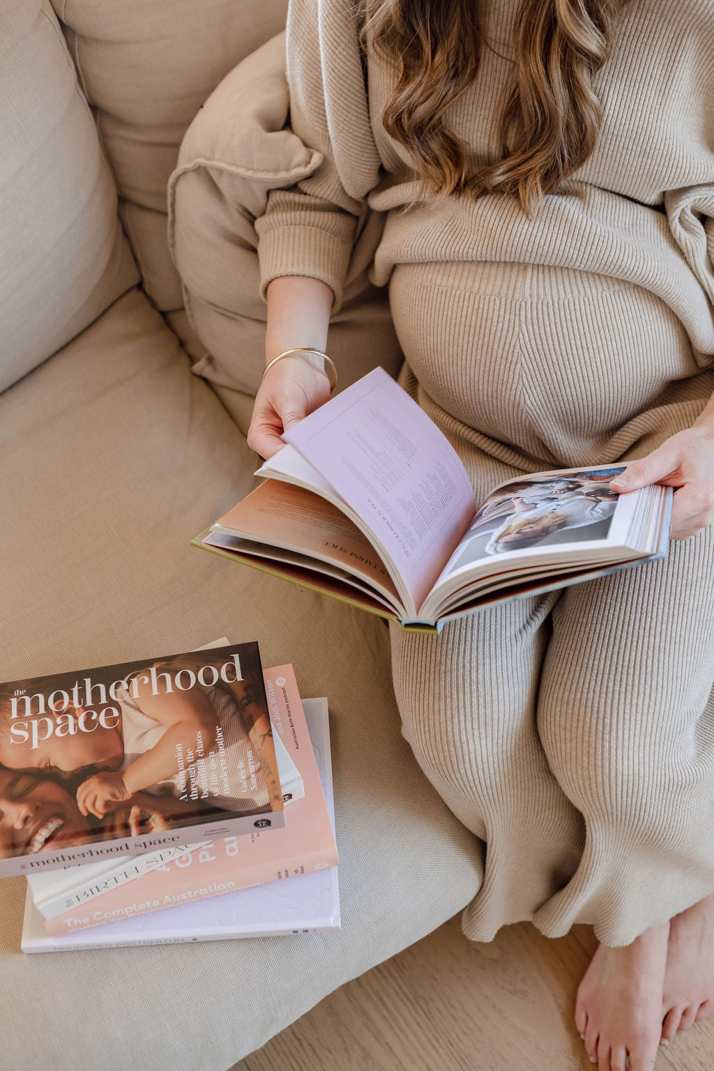 A pregnant woman reading a book on a couch.