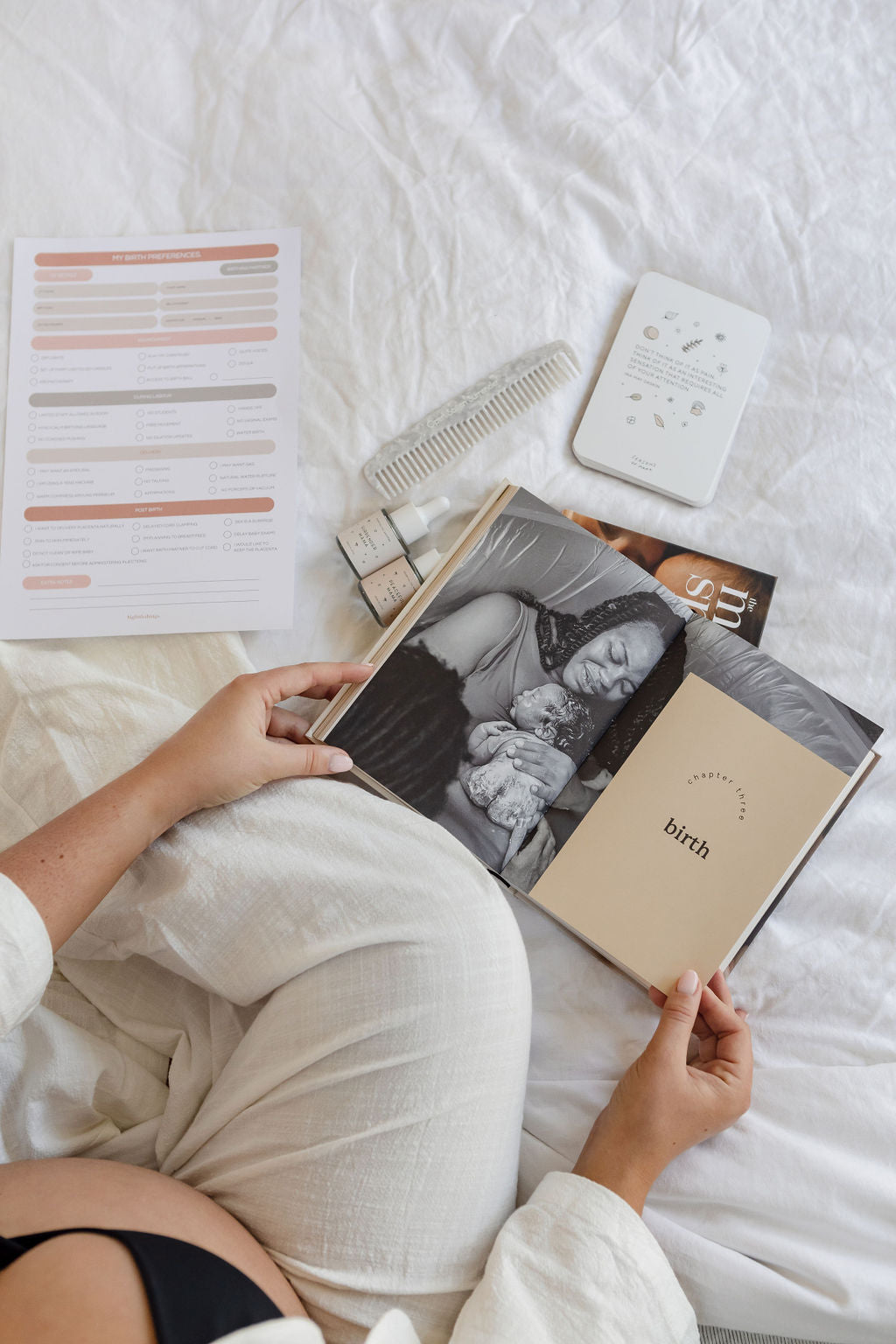 A pregnant woman reading a book on a bed.