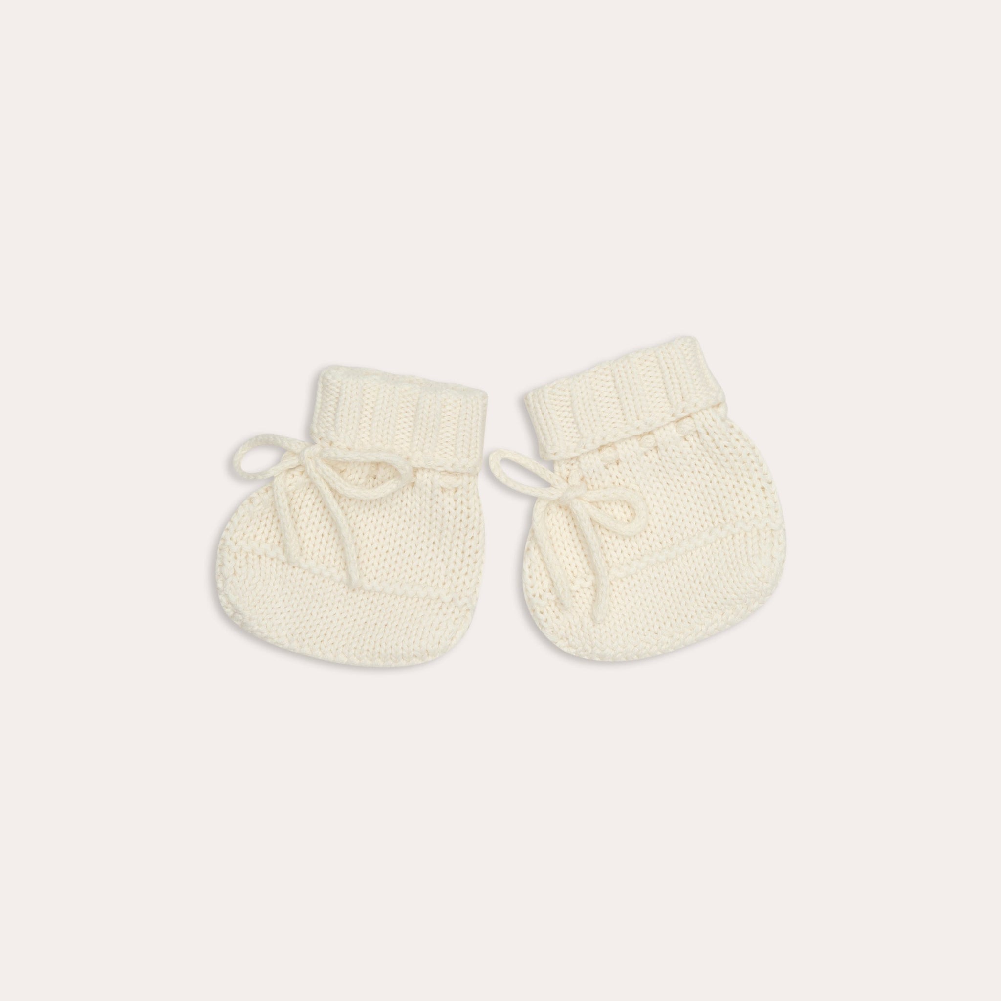 A pair of Illoura the Label knitted alba booties in vanilla on a white surface.