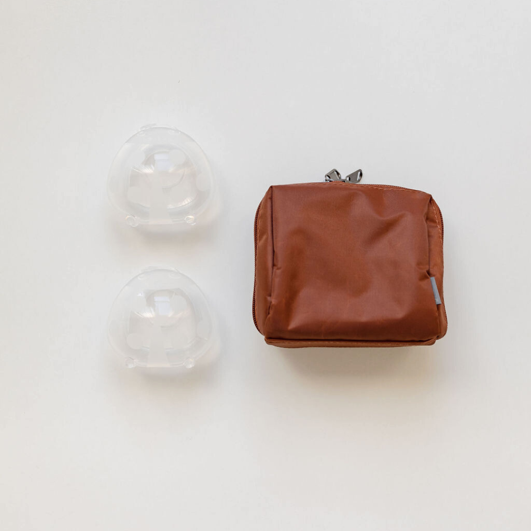 A brown bag with two Haakaa Ladybug silicone Breast Milk Collectors with Storage Bags on it.