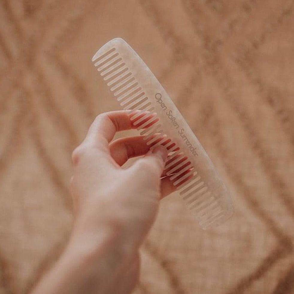 A person holding a Seasons of Mama Birth Comb on a rug.