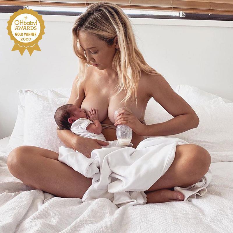 A woman is using the Haakaa Silicone Breast Pump 150ml | Gen 2 to breastfeed her baby on a bed.