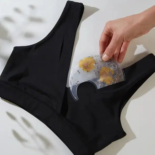 A mother is holding a black Breast Warm & Cool Insert bra top with a flower on it, by Bare Mum, for postpartum recovery.