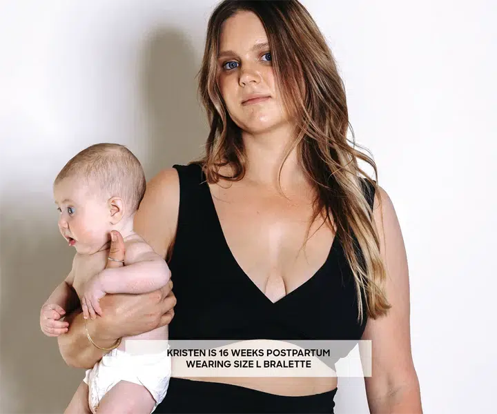 A mother breastfeeding and recovering while wearing a Bare Mum Postpartum Bralette in front of a white wall.