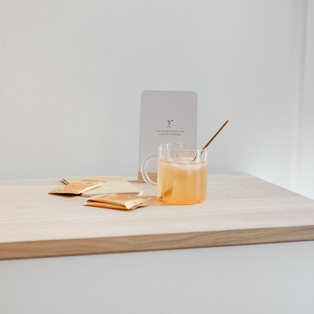 A cup of  Mini+Me. Hydramama Passionfruit + Orange with a straw on top of a wooden table.