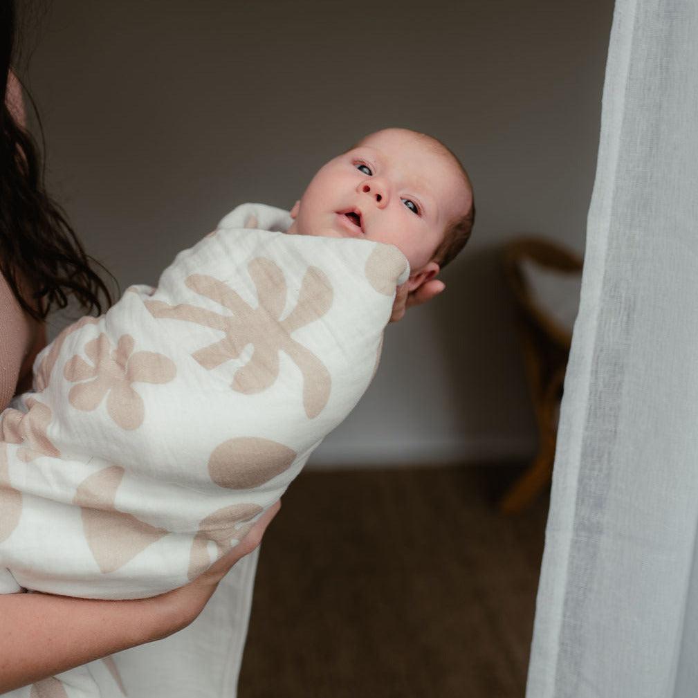A woman is holding a Bundl coastal blanket-wrapped baby.