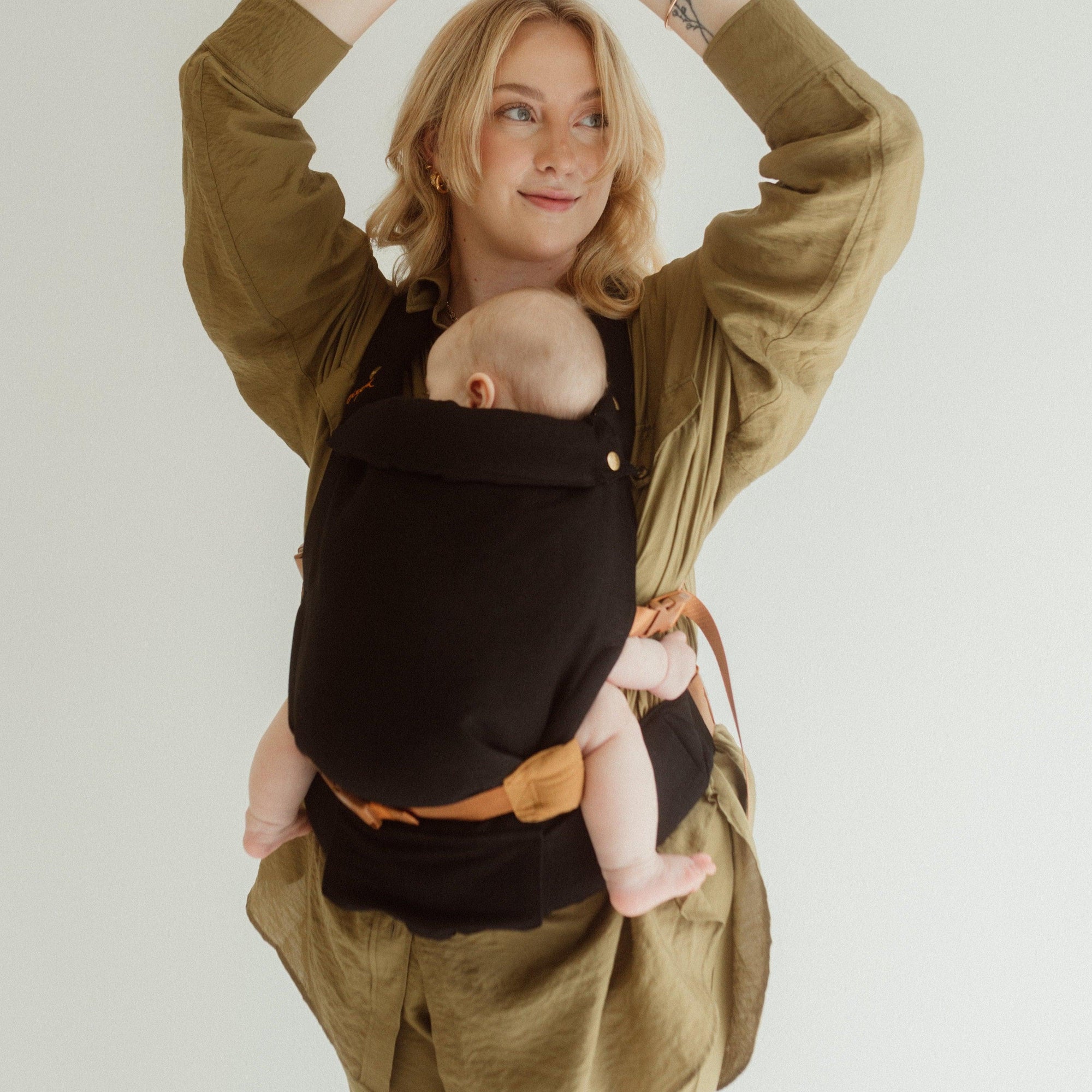 A woman wearing a Cinta Clip Carrier by Chekoh, carrying a baby.