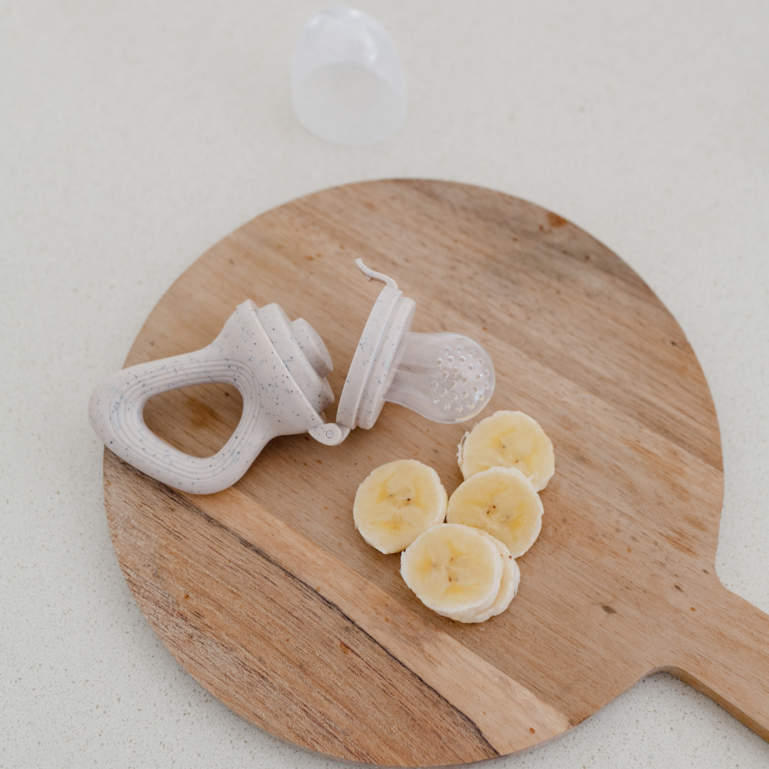 A silicone self feeder from Dove & Dovelet with slices of bananas next to it.