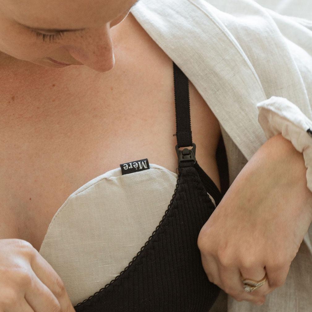 A woman is adjusting her bra straps while using Mère breast heat packs.