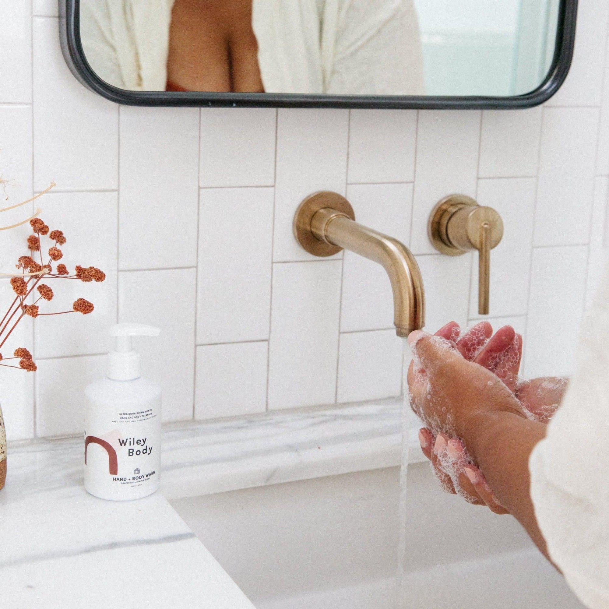 A woman using Wiley Body organic hand & body wash to cleanse her hands in front of a mirror.