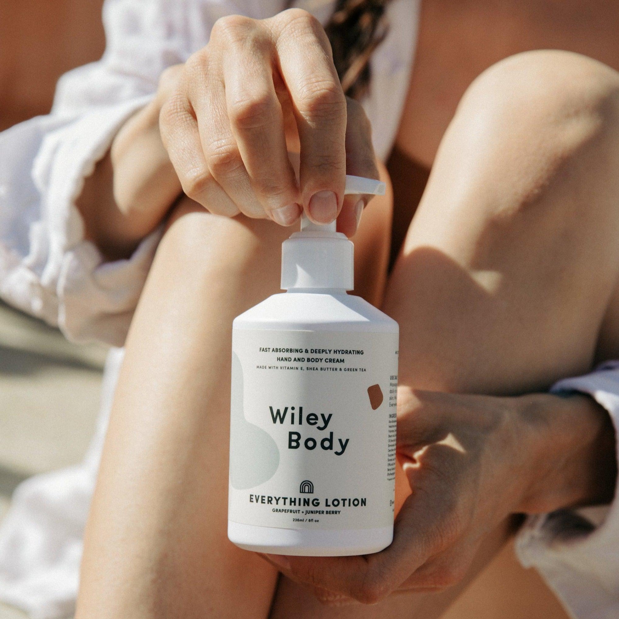 A woman is holding a lightweight bottle of Wiley Body everything lotion for hydrating her skin.