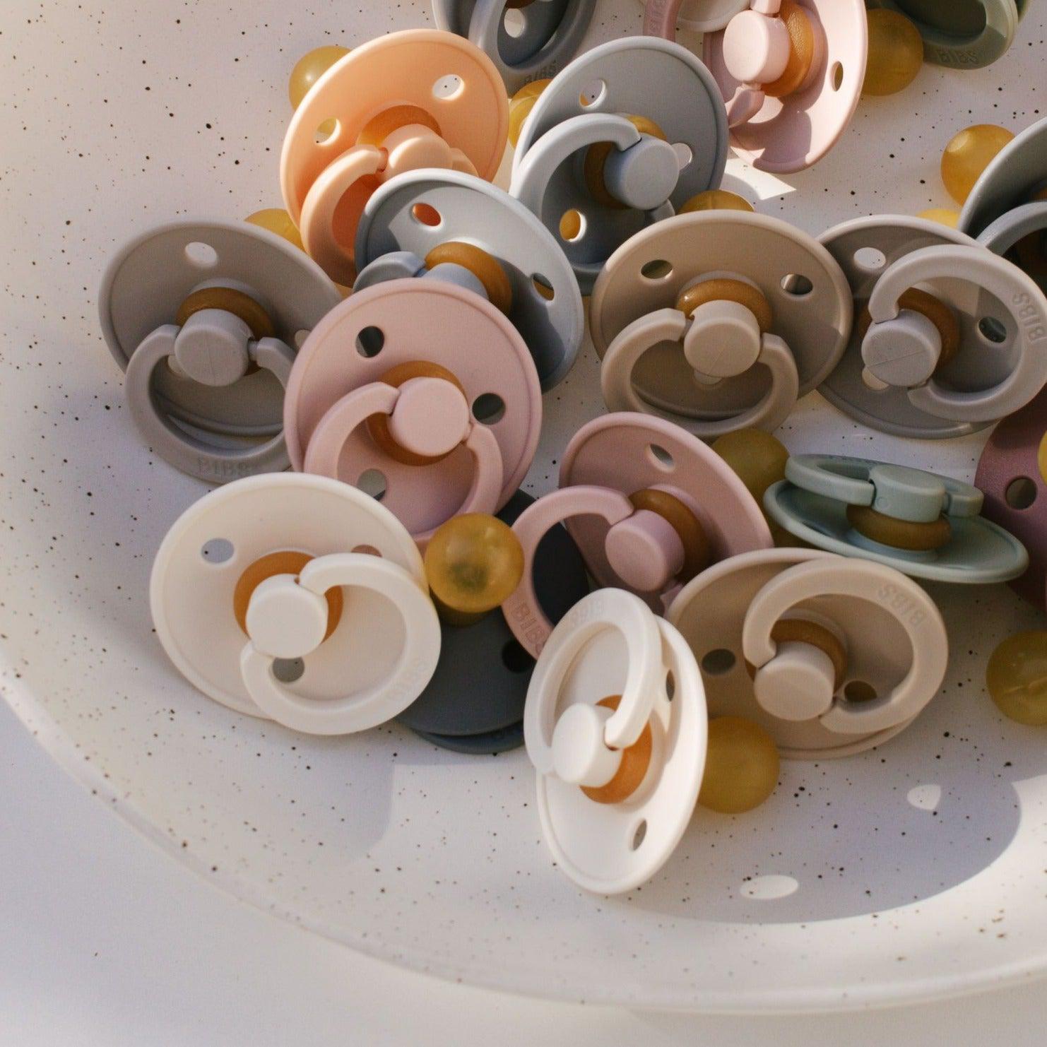 A bowl full of BIBS dummies in a variety of colours.