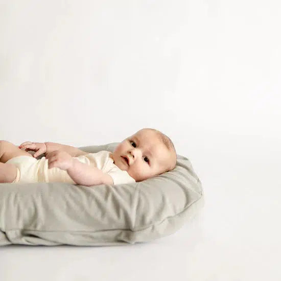 A baby snuggling on top of a Snuggle Me Lounger in the shade stone.