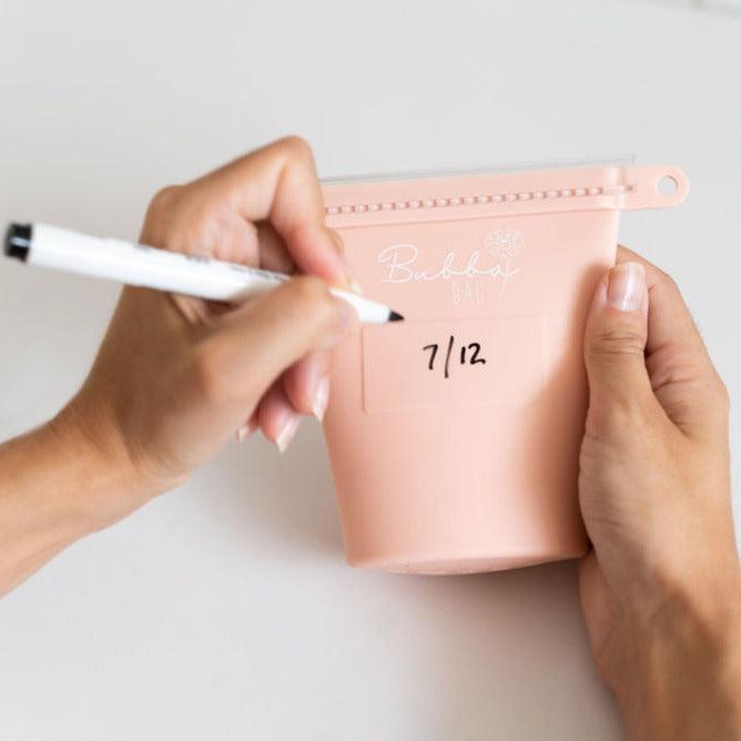 A woman writing on a bubba bag with a pen. (Brand: Marigold Baby; Product: pink bubba bags)