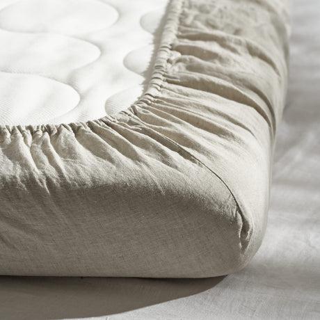 A close up of a bed with a French Linen fitted cot sheet | natural by Warren Hill.
