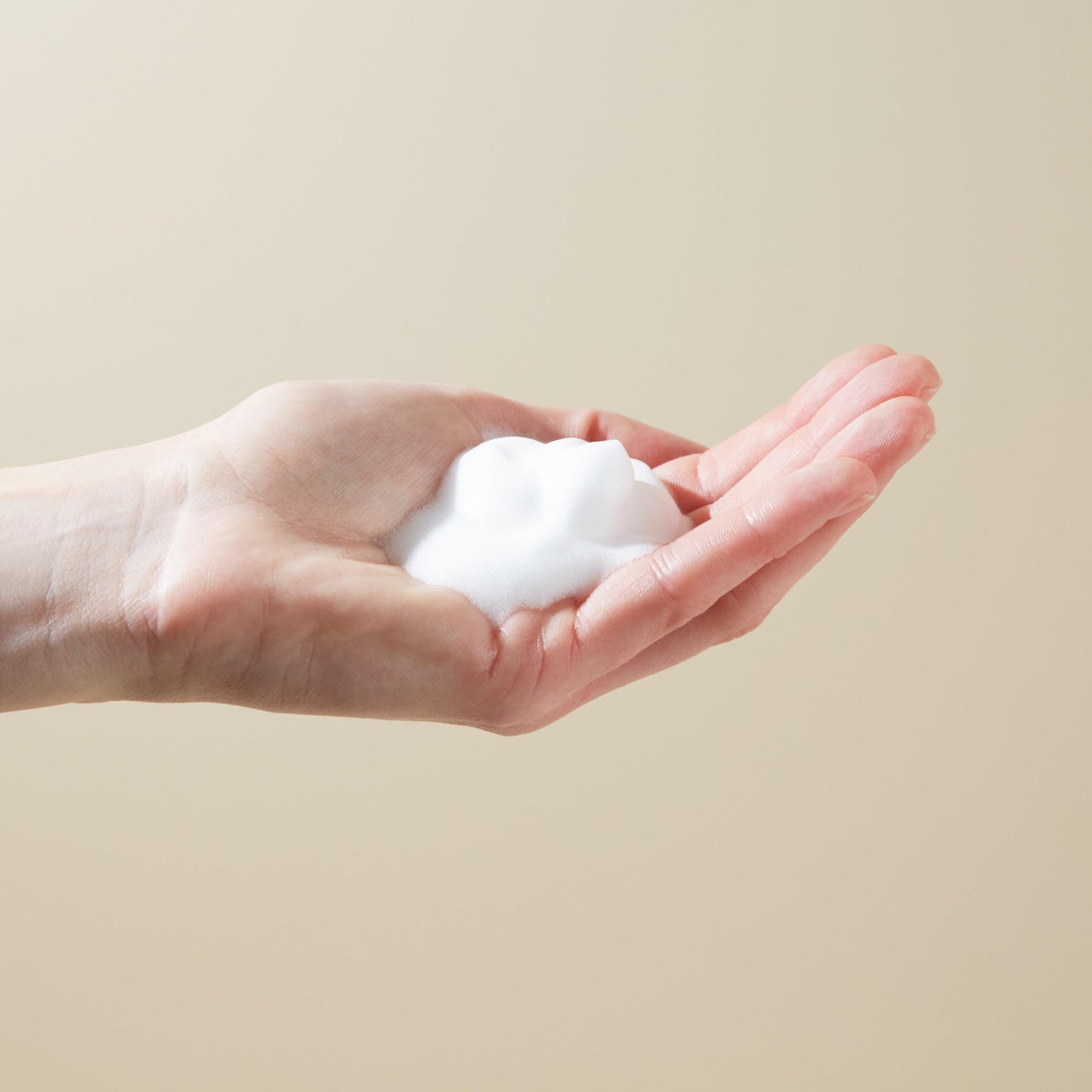 A postpartum woman's hand holding a piece of white Perineal Foam soap from Bare Mum on a beige background.