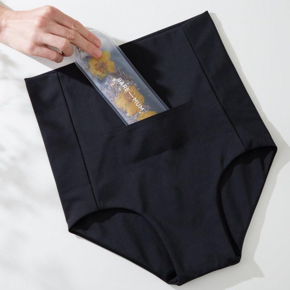 A mother is holding a black Postpartum Briefs with a Warm & Cool Insert for recovery after giving birth.