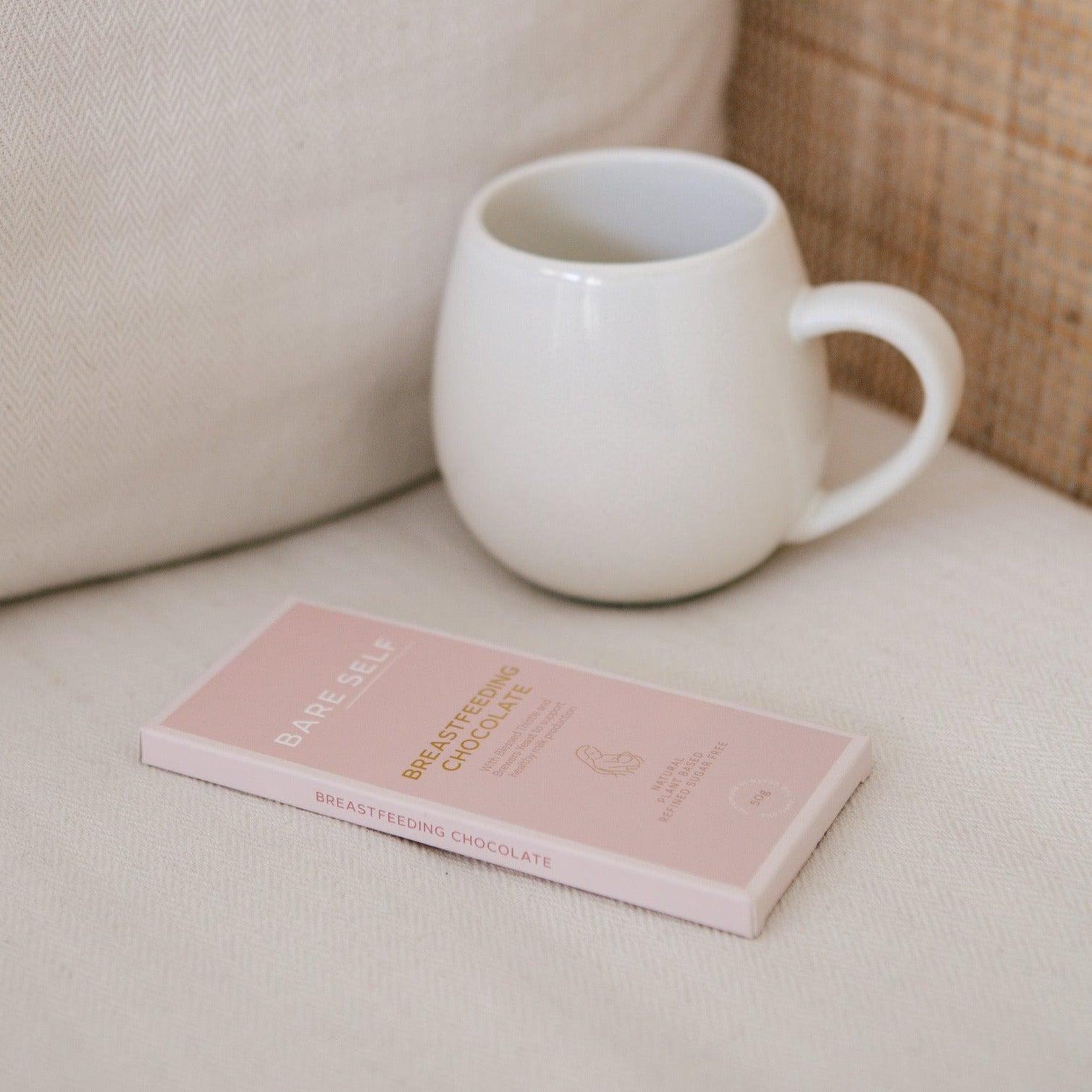 A cup of Bare Self coffee and a Bare Self breastfeeding chocolate bar on a white couch.