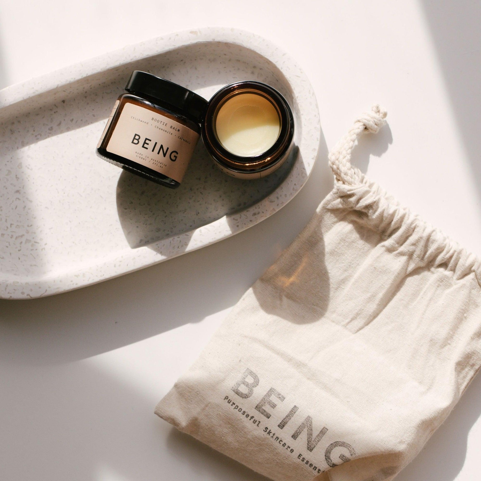 A small container with a  Being Skincare balm duo set and a bag on a white table.