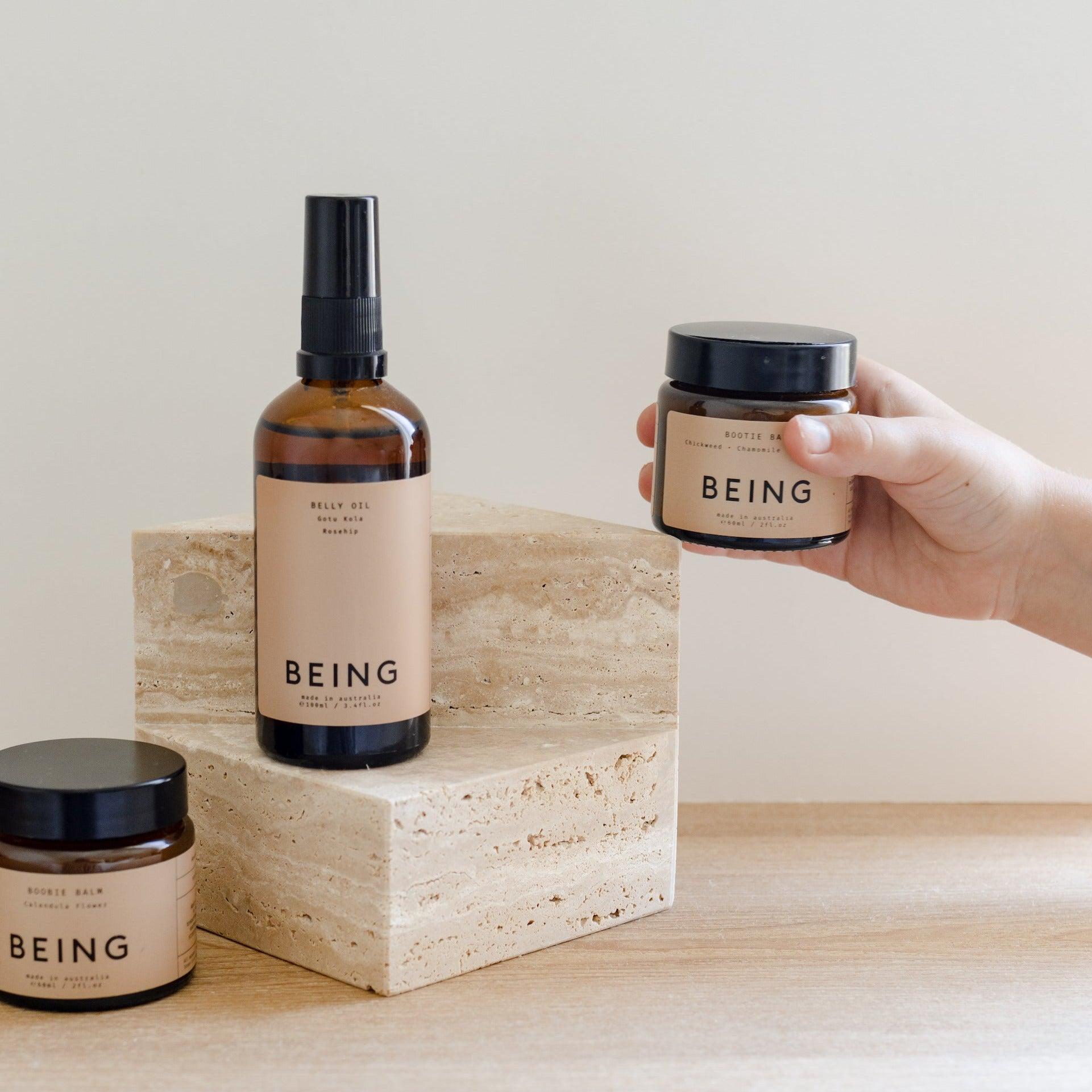 A hand holding a jar of Being Skincare's Bootie balm.