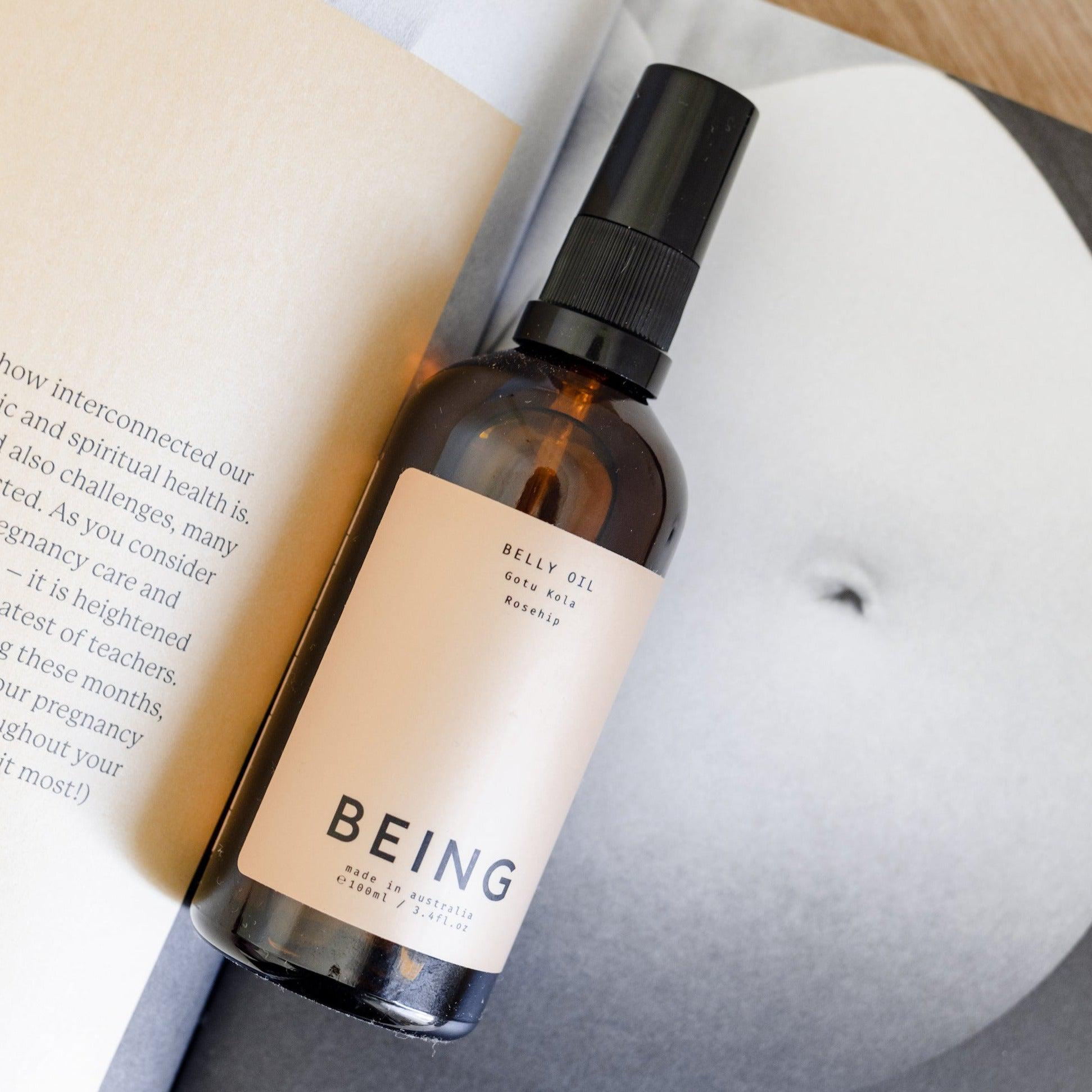 A bottle of Being Skincare Belly Oil next to a book. 