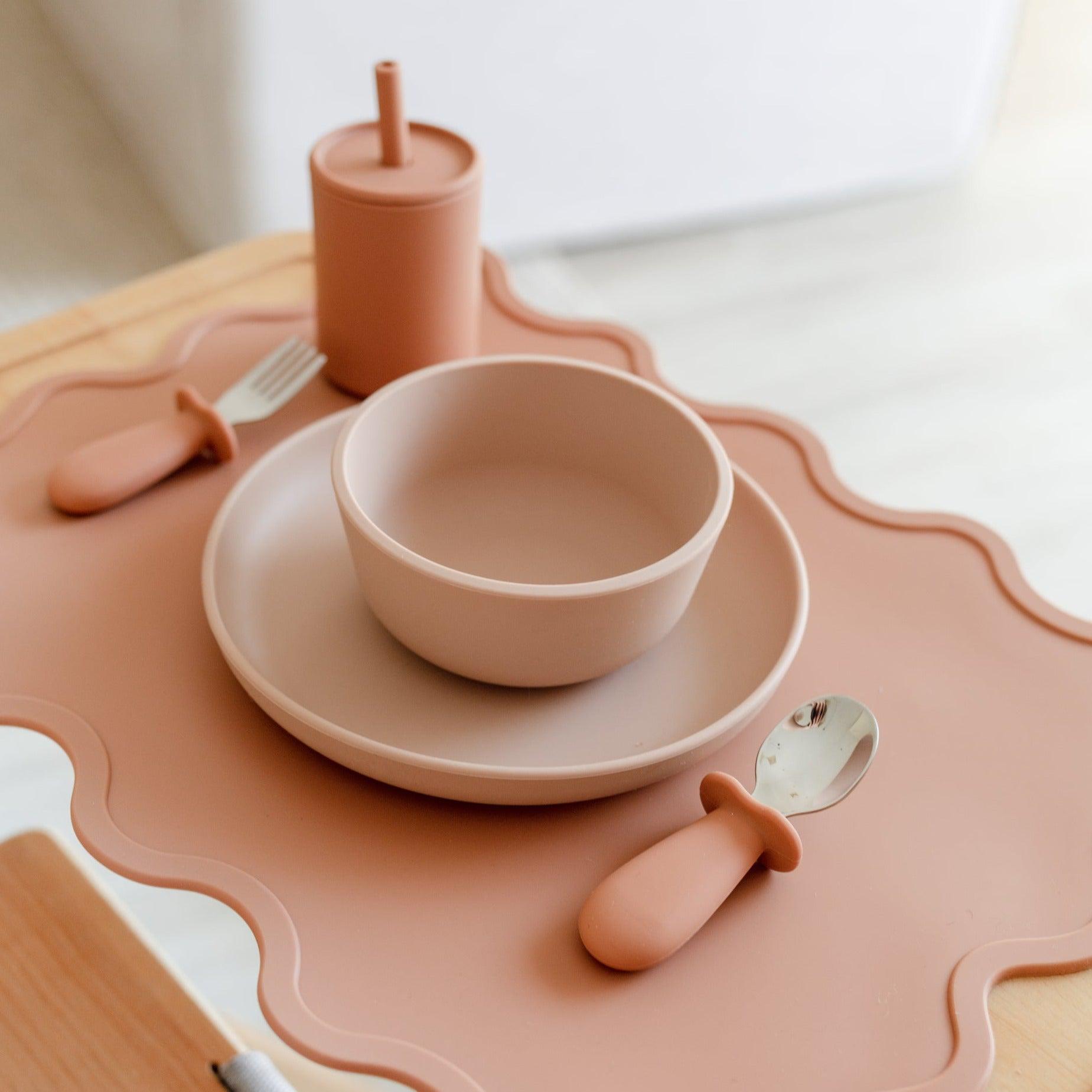 A Wiggly Placemat in cinnamon by Rommer, with a pink plate, spoon, and fork on a table.