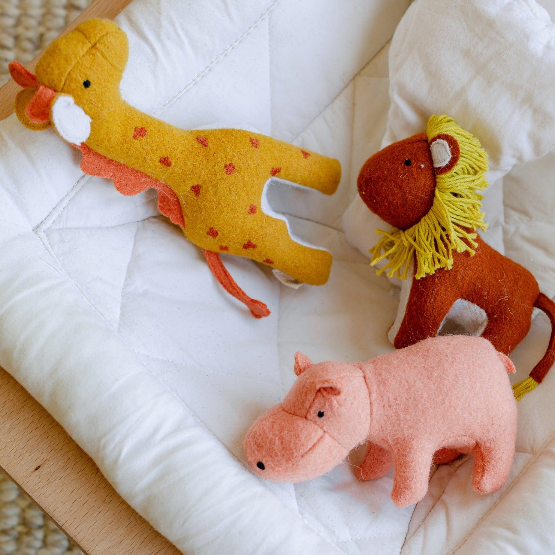 In the savannah, a Holdie Folk - Savannah Animals set from Olli Ella, consisting of a giraffe and a zebra, peacefully rests on a bed while accompanied by a hippo.