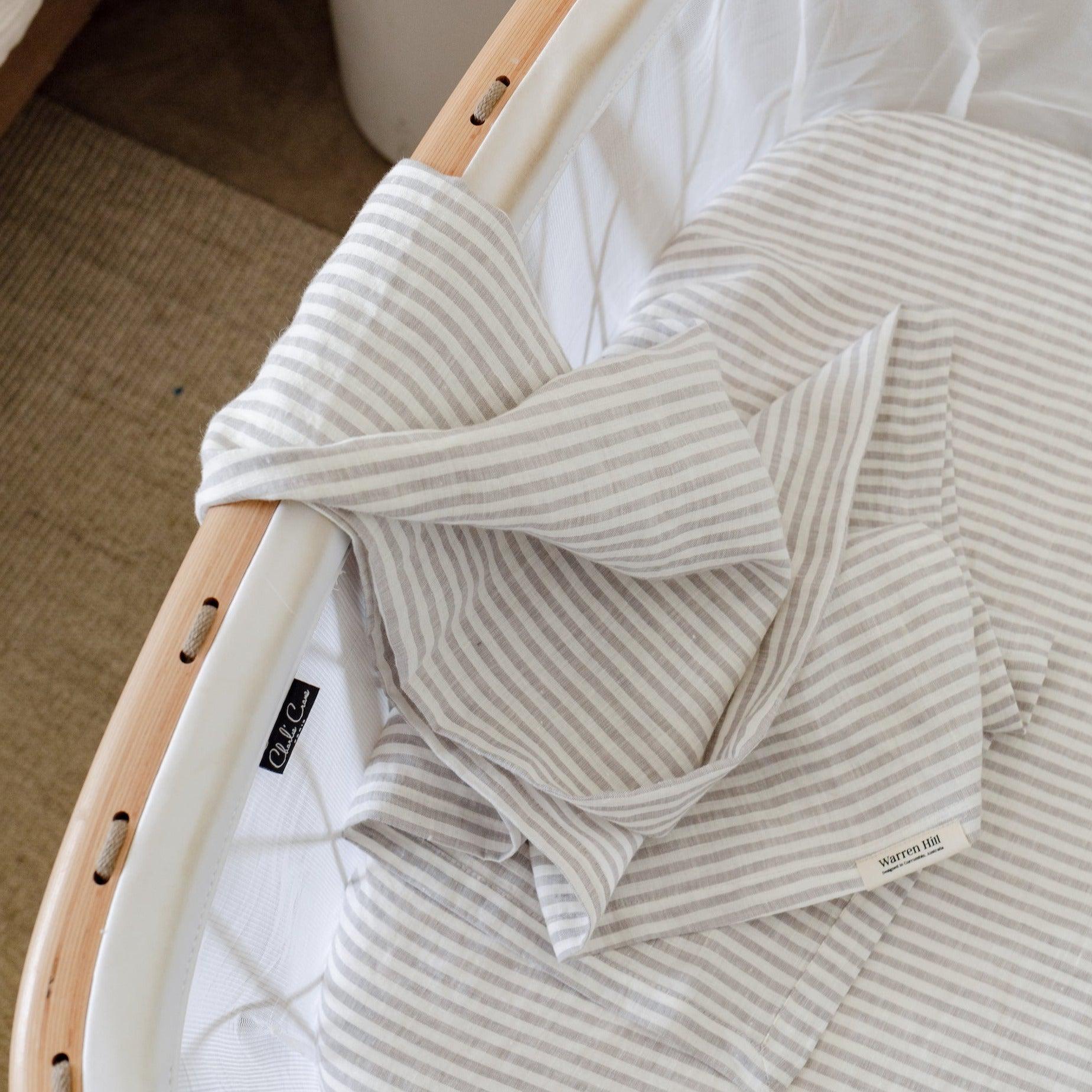 A white and grey striped french linen baby swaddle by Warren Hill in a crib made with breathable stonewashed linen.