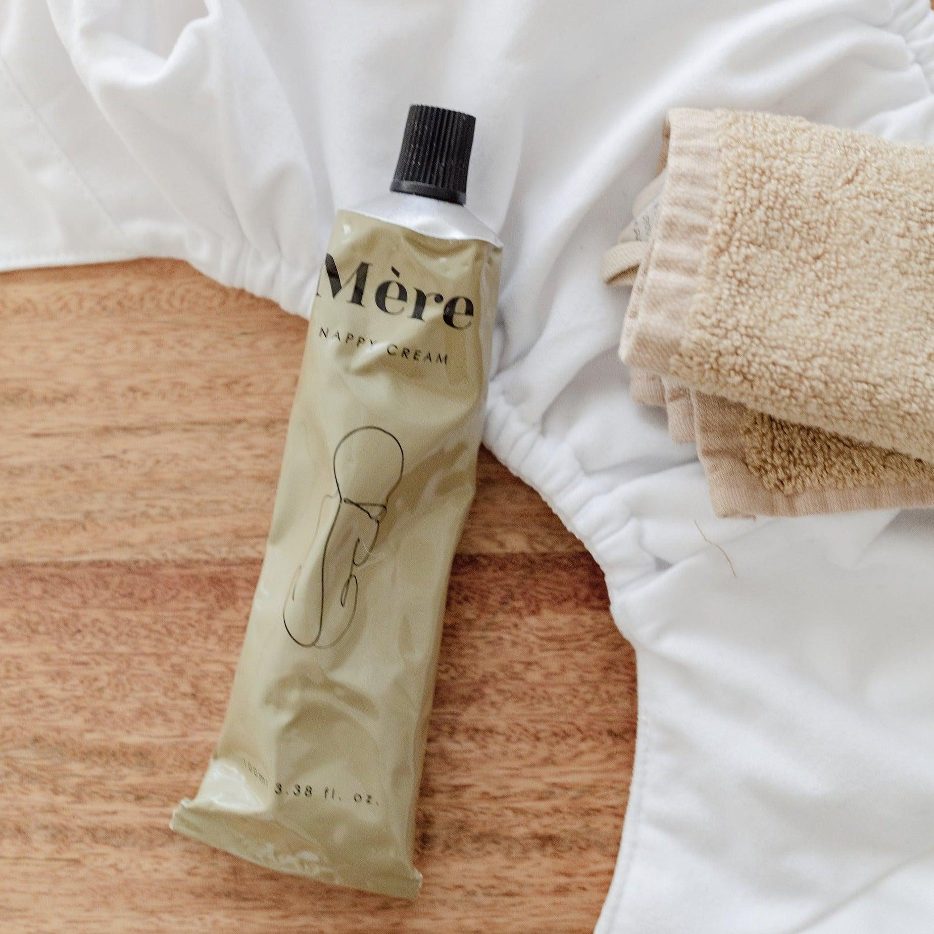A bottle of Mère Nappy Cream and a towel on a wooden table.