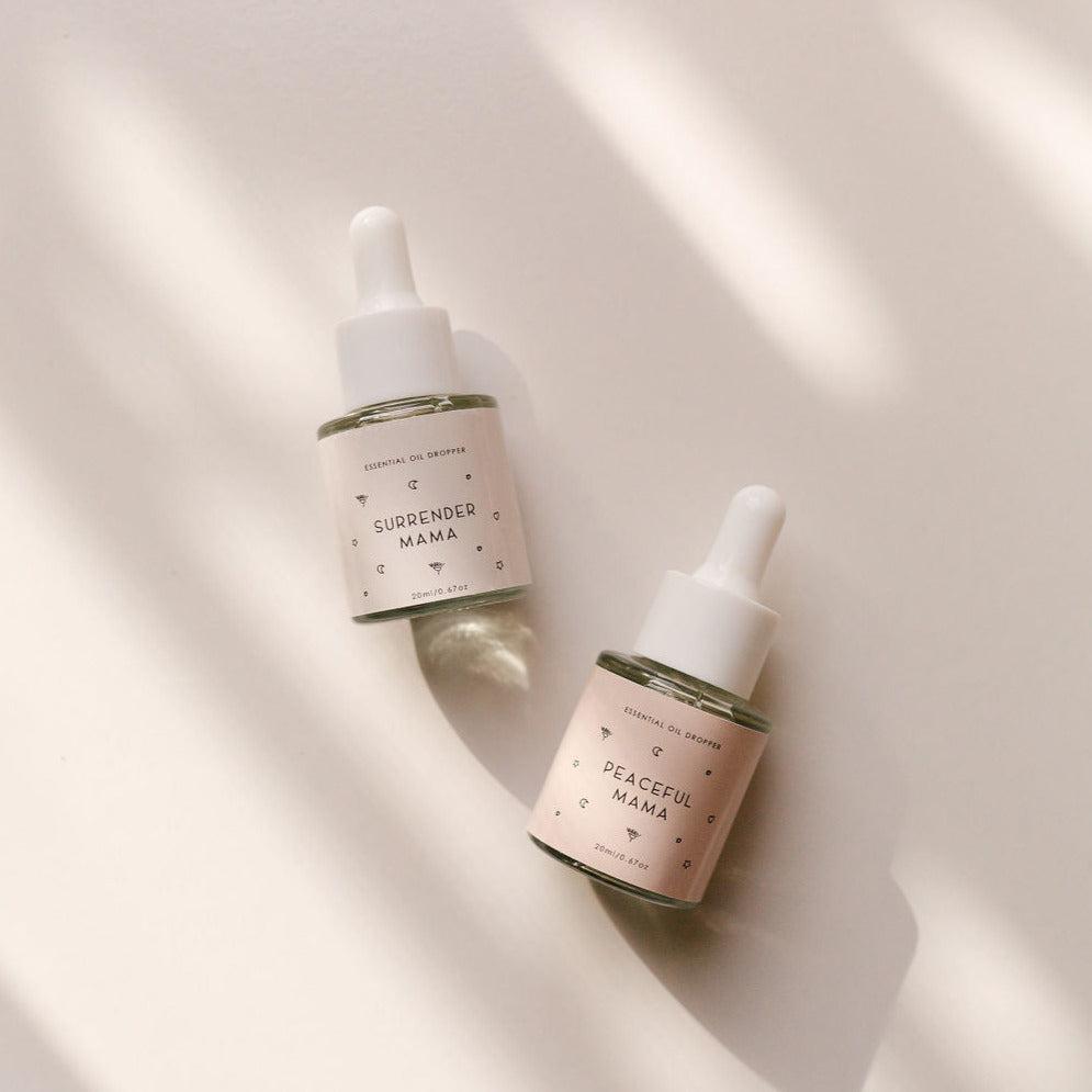 Two small bottles of Seasons of Mama Essential Oil Duo including Surrender Mama and Peaceful Mama on a white surface.
