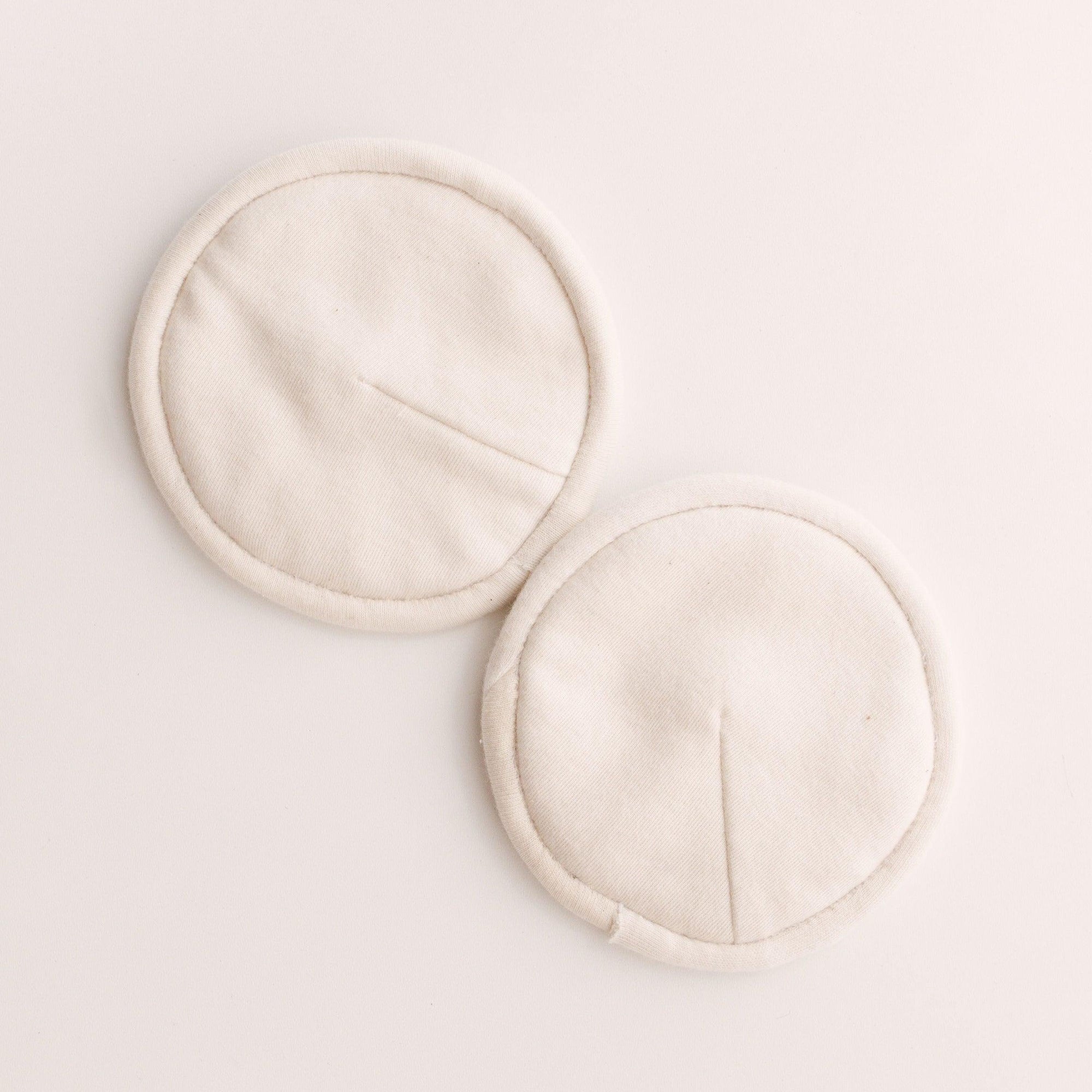 Two Bundl. white cloth breast pads on a white surface.