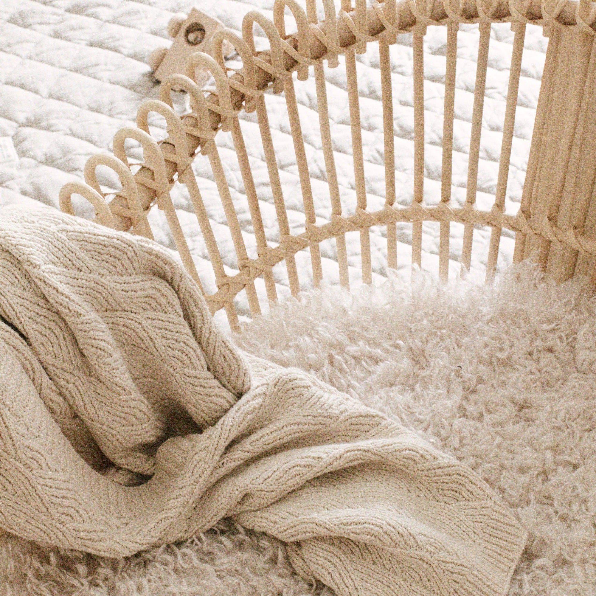 A wicker basket with a Bundl. Organic Cotton Blanket on top.