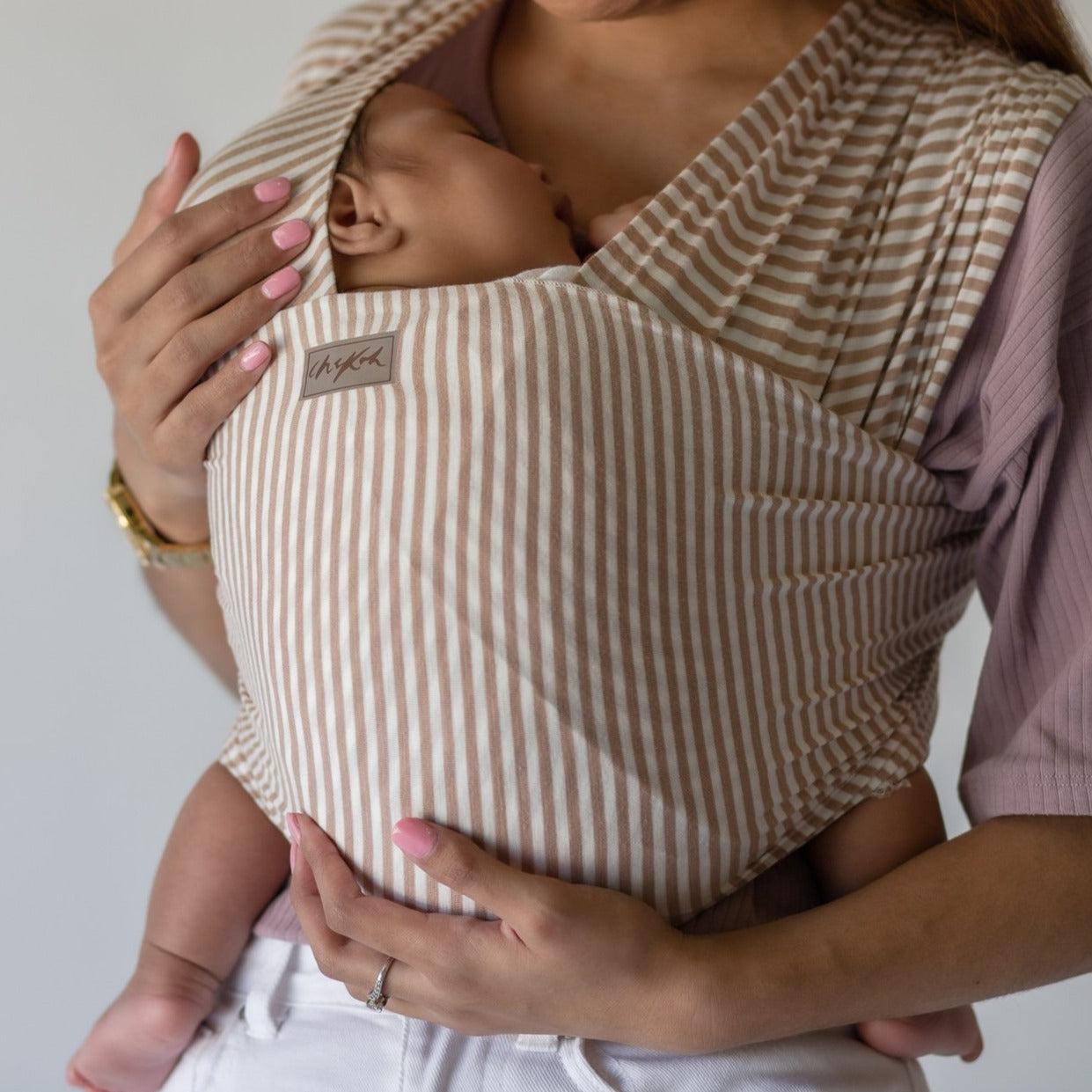 A woman holding a baby in a Cinta Stripe Wrap by Chekoh.