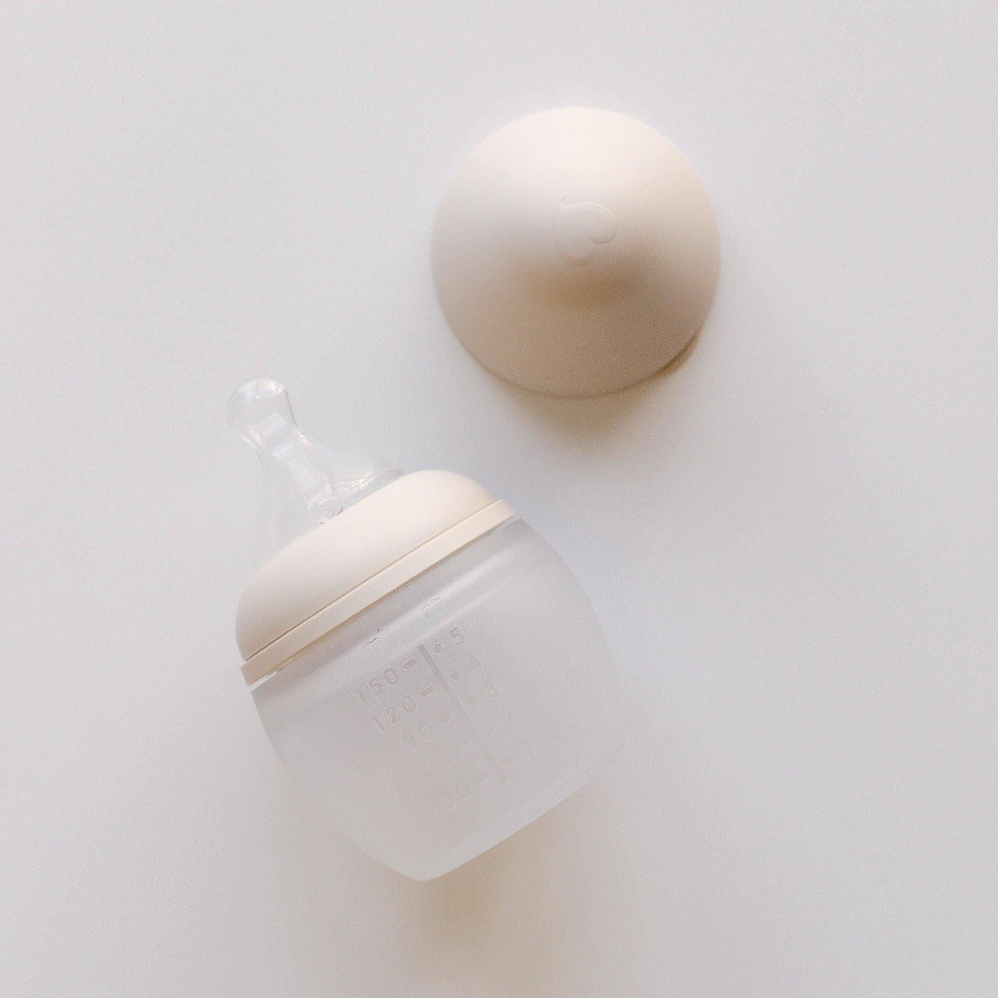 An Elhée France baby bottle in the shade sand laying on a white surface.