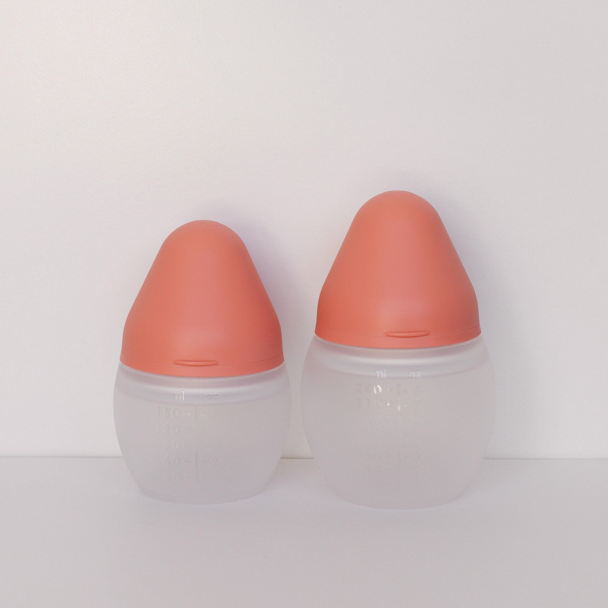 Two BibRond summer coral baby bottles by Elhée France standing against a white surface.