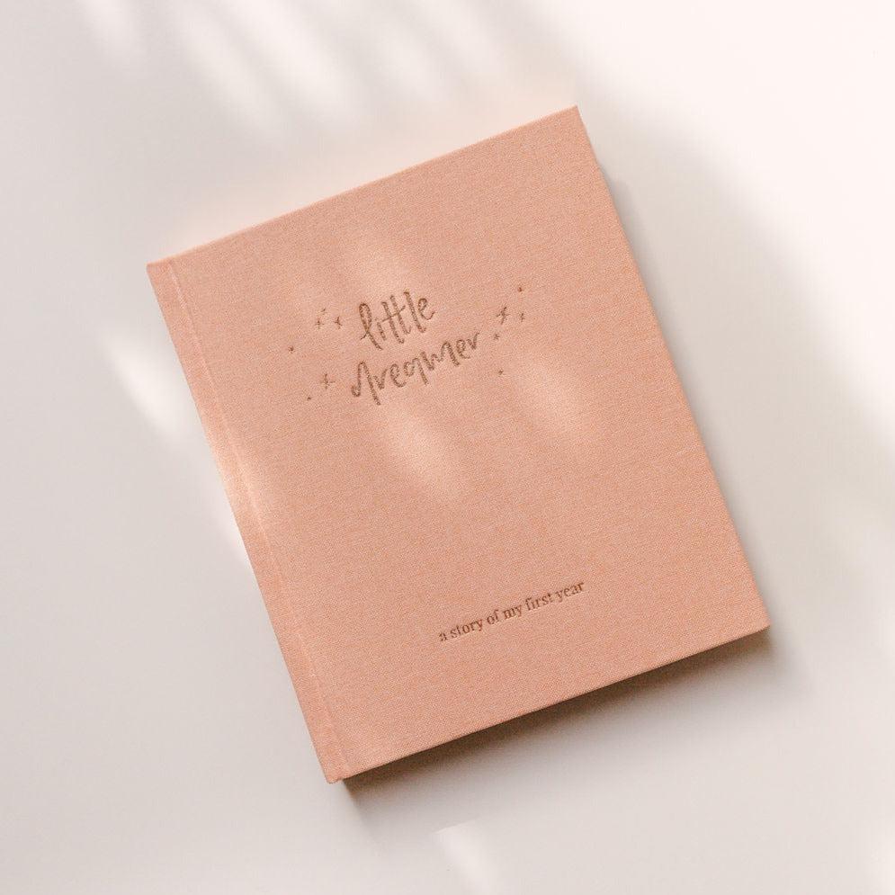 An Emma Kate Co. little dreamer baby journal in the shade petal on a white surface.