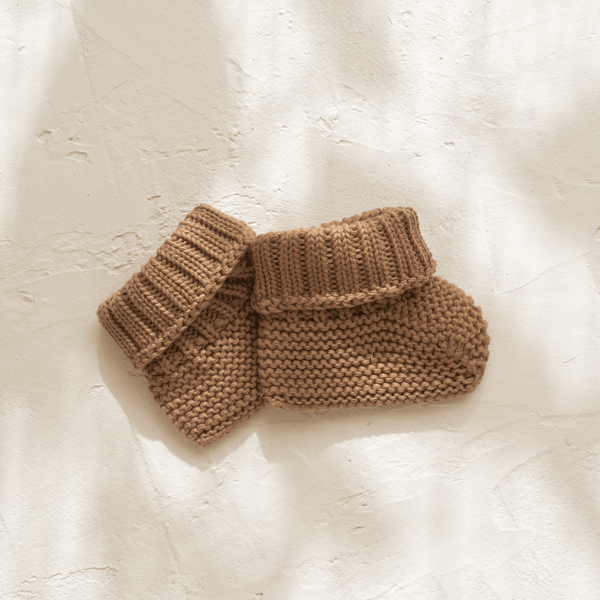 A pair of Illoura the Label organic cotton knitted illoura baby booties in chocolate on a white surface.