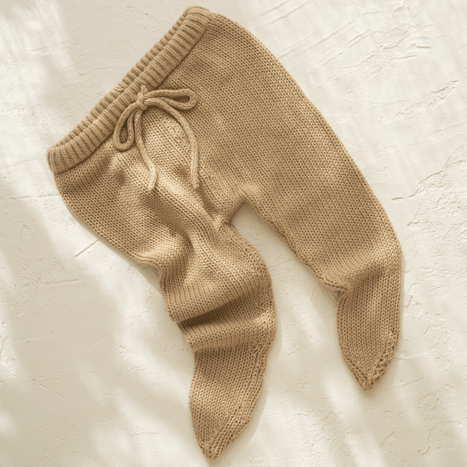 A pair of Illoura the Label's illoura poet pants in olive, made of beige organic cotton, laying on a white surface.