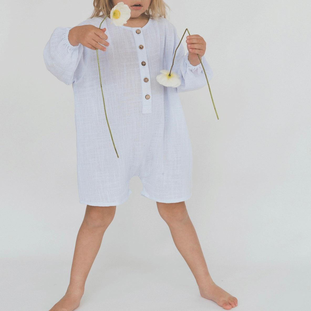 A little girl in an Illoura the Label husk romper in powder blue holding flowers.