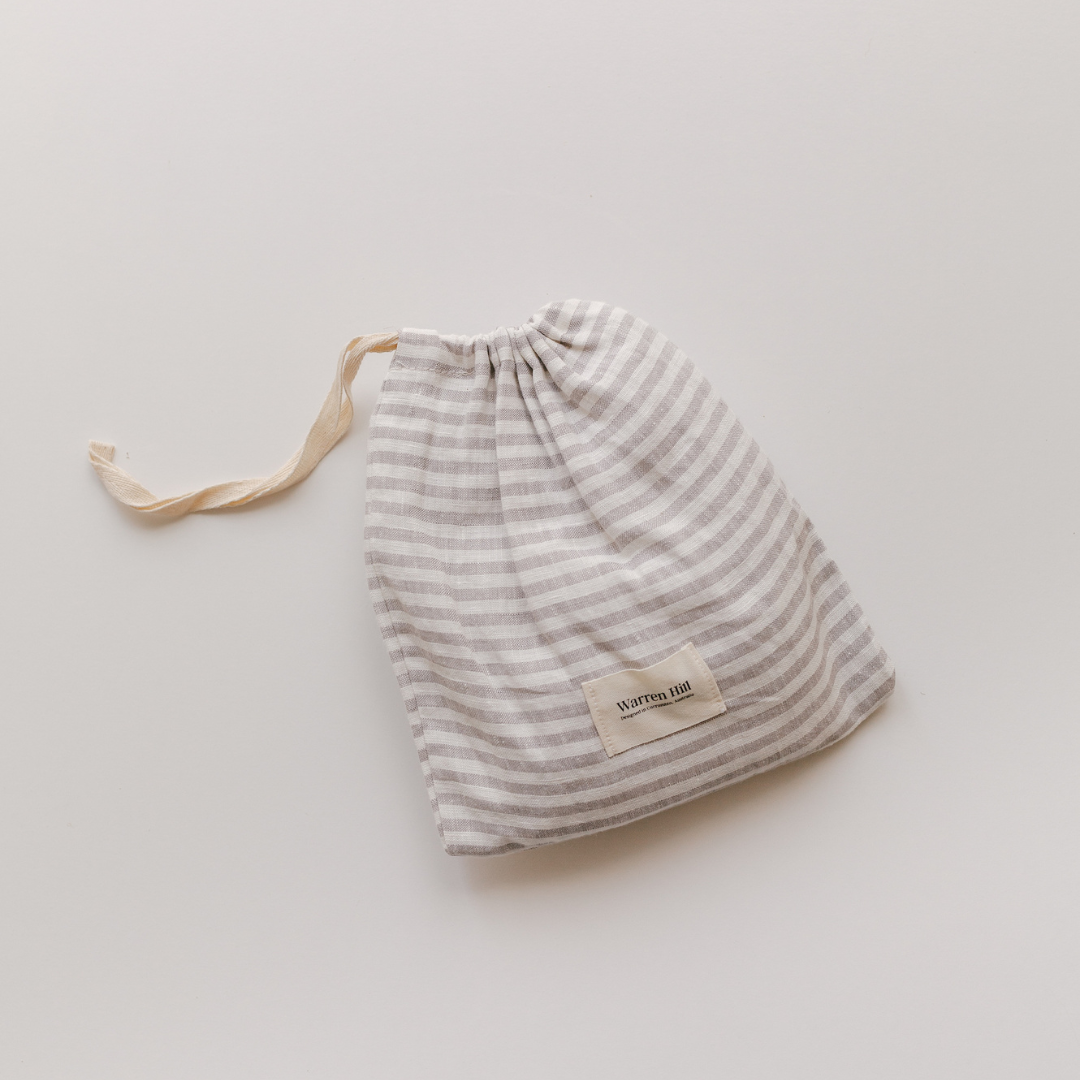 A grey and white striped French Linen Fitted Bassinet Sheet by Warren Hill on a white surface in a neutral nursery.