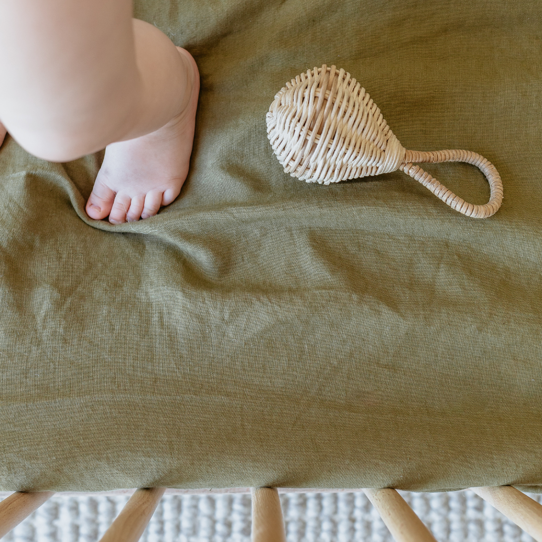 A baby's feet on a Warren Hill french linen fitted cot sheet in a neutral nursery.