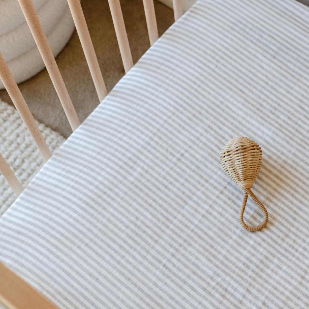 A baby crib with striped bedding and Warren Hill french linen fitted cot sheets in grey stripe.