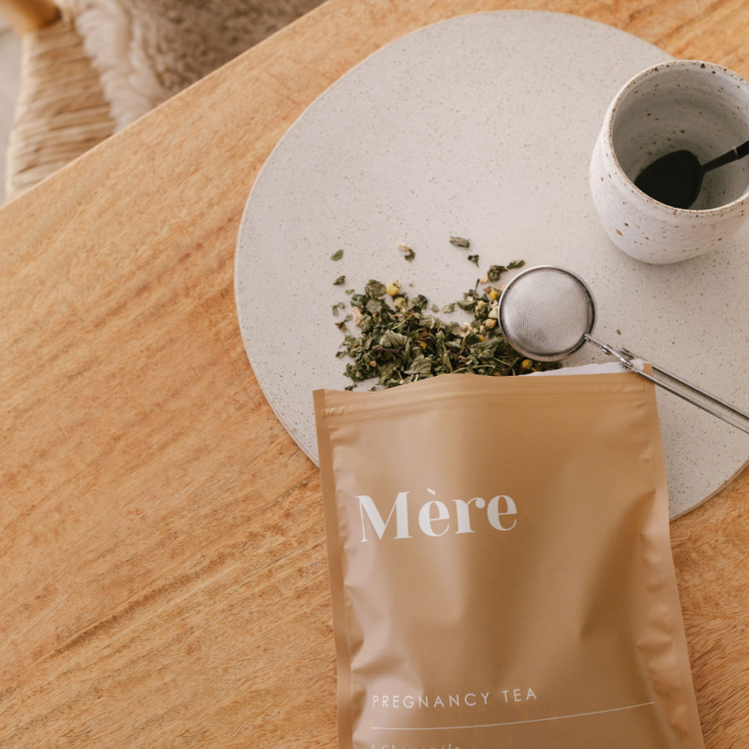 A bag of Mère Organic Pregnancy Tea on a table next to a mug.