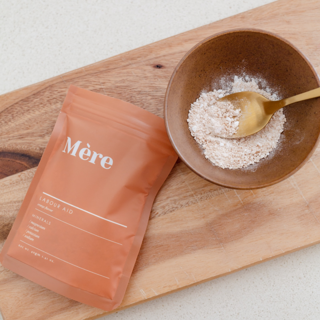 A bag of Labour Aid powder next to a wooden cutting board by Mère.