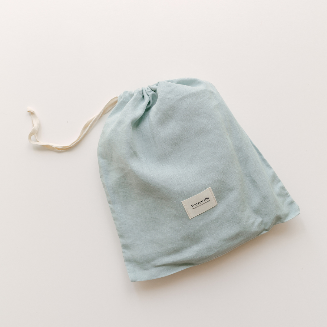 A blue drawstring bag on a white surface, perfect for organizing Warren Hill french linen fitted cot sheets in aqua color or storing fitted cot sheets in a neutral nursery.