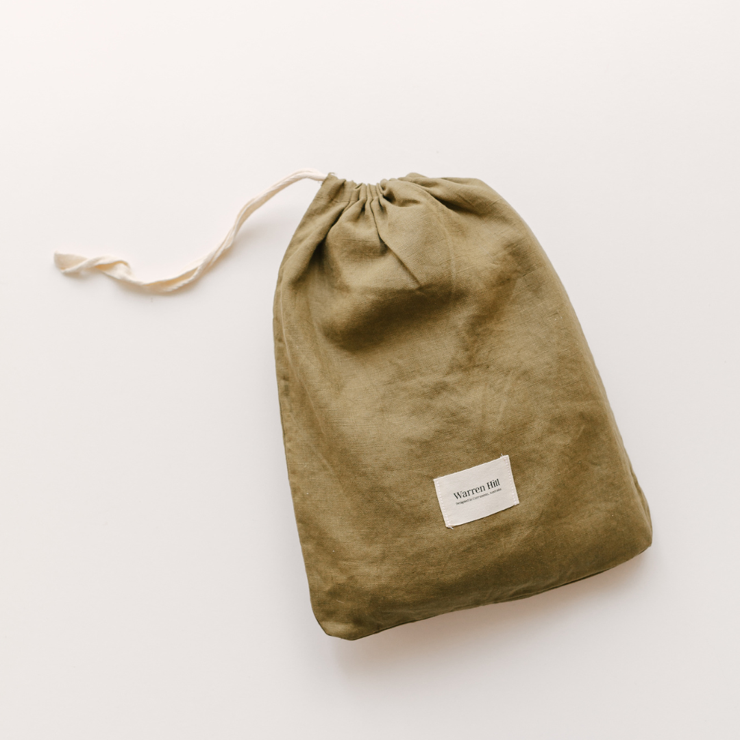 A Warren Hill french linen fitted cot sheet in olive green, on a white surface, perfect for a neutral nursery.